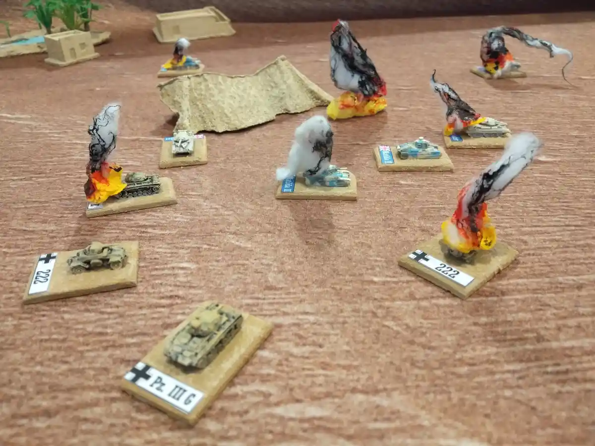 A tabletop wargame scene shows numerous miniature tanks on wooden bases, many of which are visibly destroyed with painted…