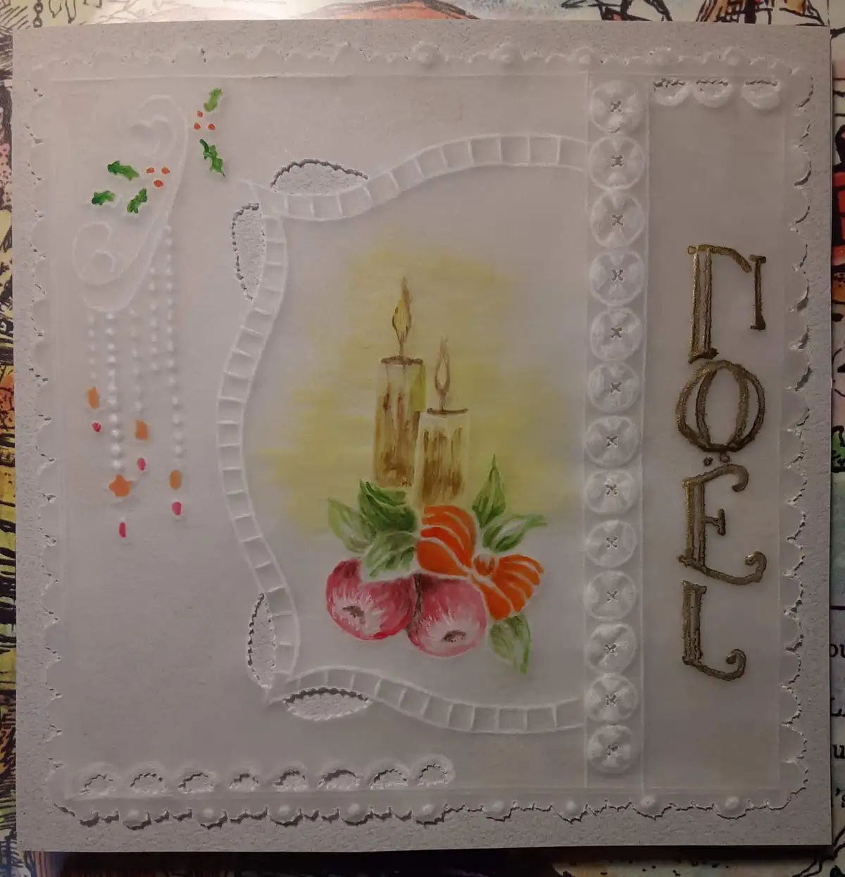 A handmade Christmas card with embossed white borders and a central watercolor illustration of two lit candles, red apples…