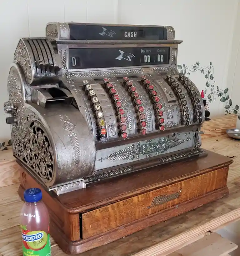 An ornate, vintage National brand mechanical cash register with a 'CASH' display and 'Dollars Cents' readout showing '00…
