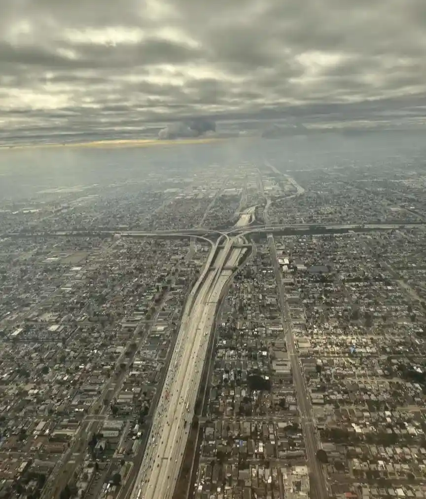 An aerial view from an airplane window shows a sprawling urban landscape dominated by a massive highway interchange cutting…