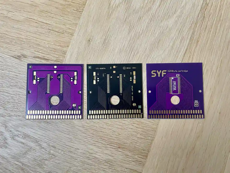 Three purple and black printed circuit boards, likely from Sega Genesis game cartridges, are laid out on a light wood…