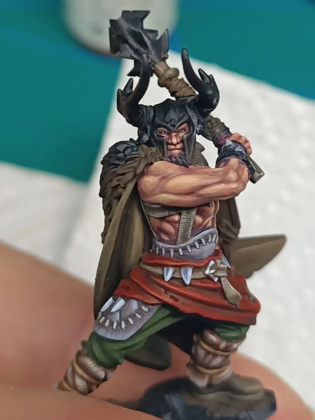 A hand-painted miniature figurine of a muscular, horned warrior in fantasy armor, holding a large axe over his shoulder…