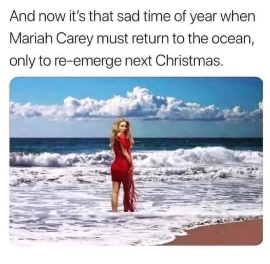 A woman with blonde hair wearing a red dress stands in shallow ocean water with waves breaking around her. The sky is blue…