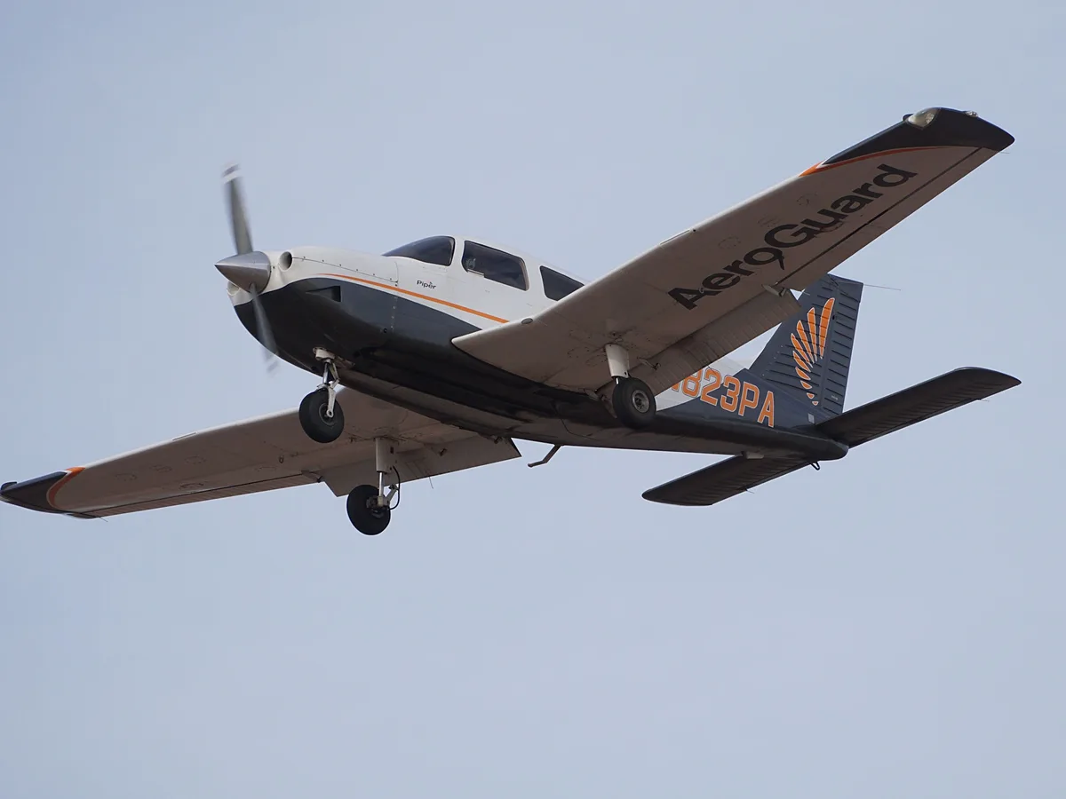 A white and grey Piper single-engine propeller airplane with 'AeroGuard' written on its wing and 'N823PA' on its tail is…