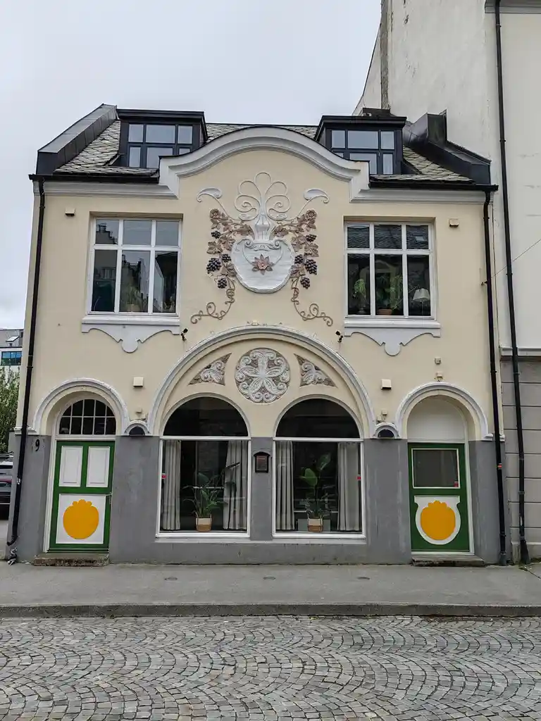 a photograph of a cream-colored building with ornate architectural details, including arched windows and decorative floral…