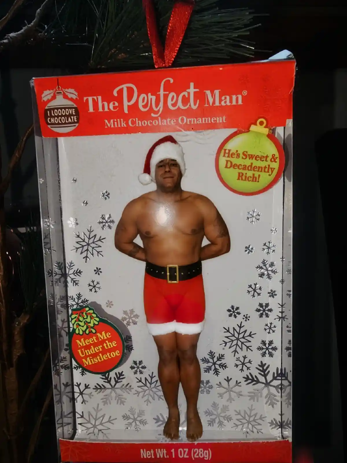 A packaged milk chocolate ornament shaped like a shirtless, muscular man wearing a Santa hat and red shorts with white trim…