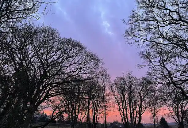 A photograph of a vibrant sunset or sunrise with a gradient sky transitioning from pink and orange near the horizon to…