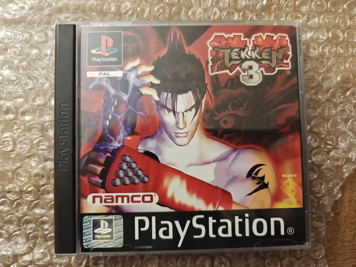 A physical PlayStation game case for Tekken 3, featuring artwork of a male fighter with red gloves and lightning effects…