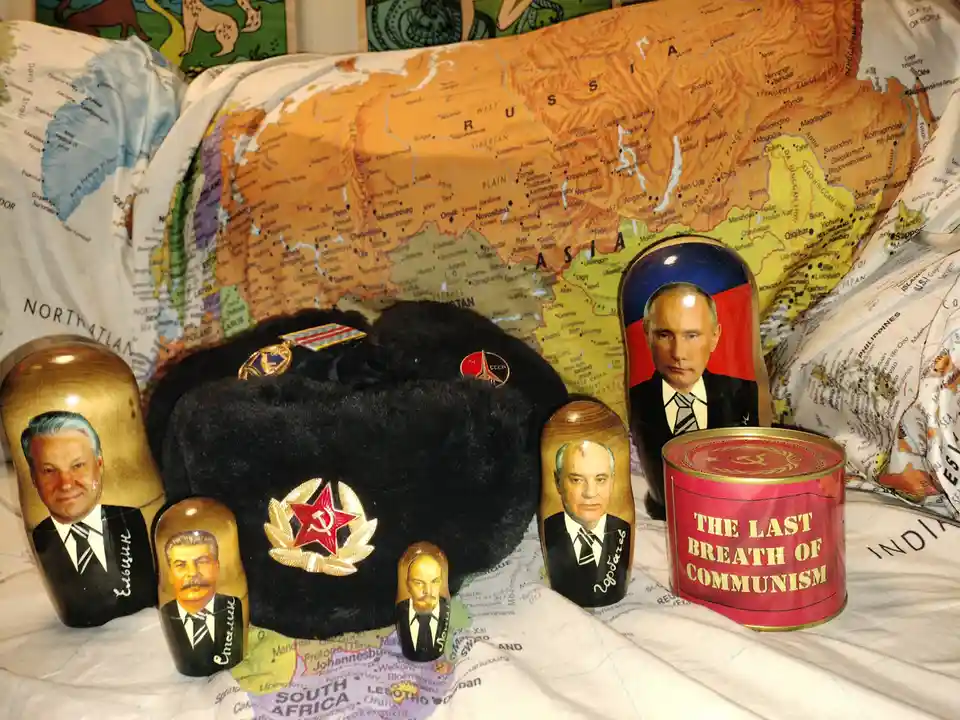 A collection of Russian-themed items including a black ushanka hat with a red star and hammer-sickle emblem, several…