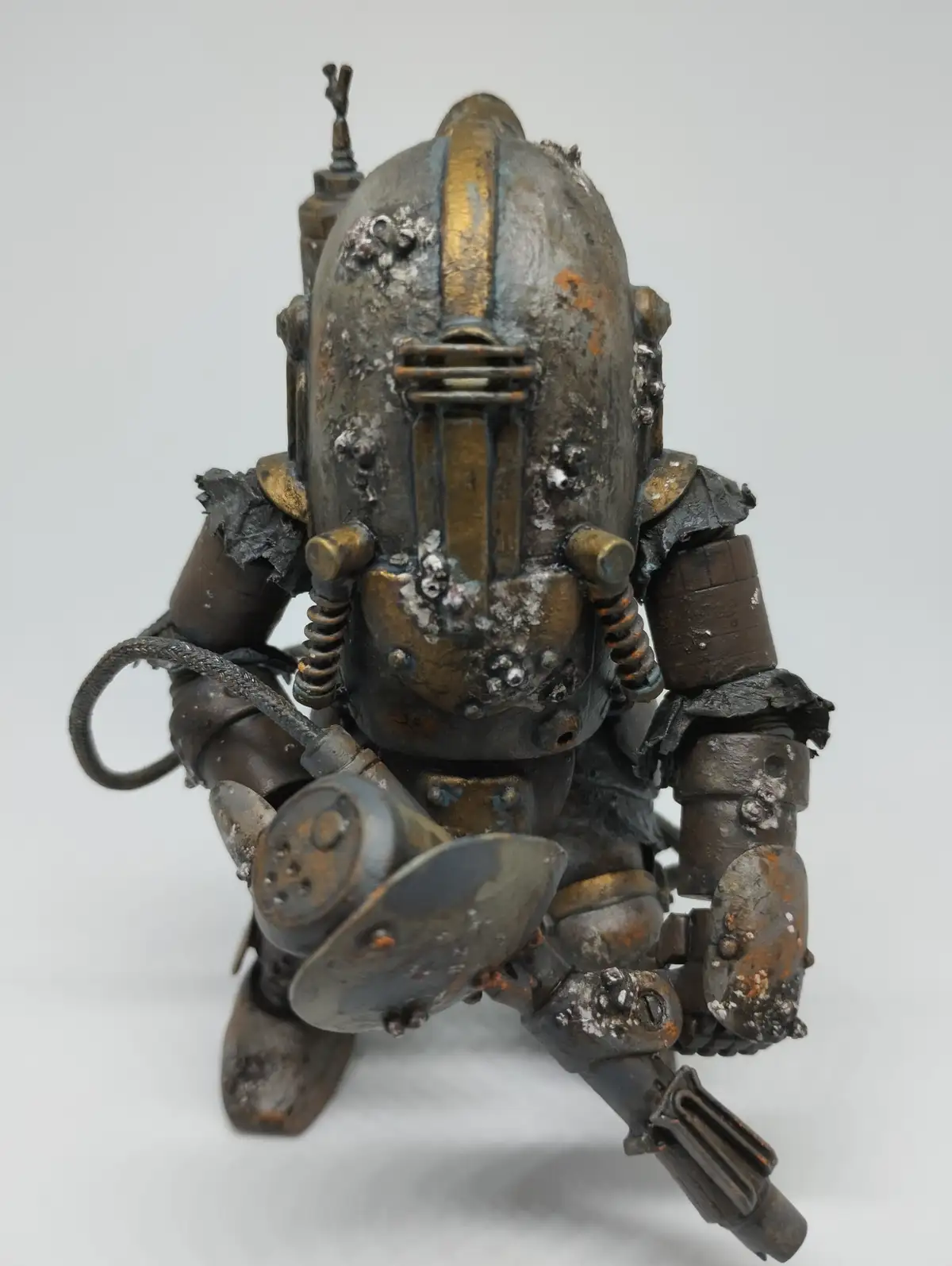 A heavily weathered, rusted, and dented action figure of a Power Armor suit from Fallout, crouching with a weapon, overlaid…