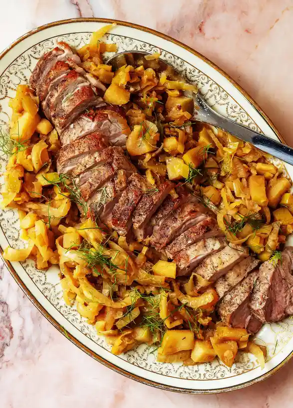A beautifully plated dish of sliced roasted meat, likely pork, served with sautéed onions and diced potatoes, garnished with…