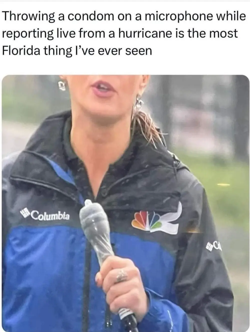 A female news reporter wearing a blue and black Columbia jacket with an NBC logo is holding a microphone wrapped in a…
