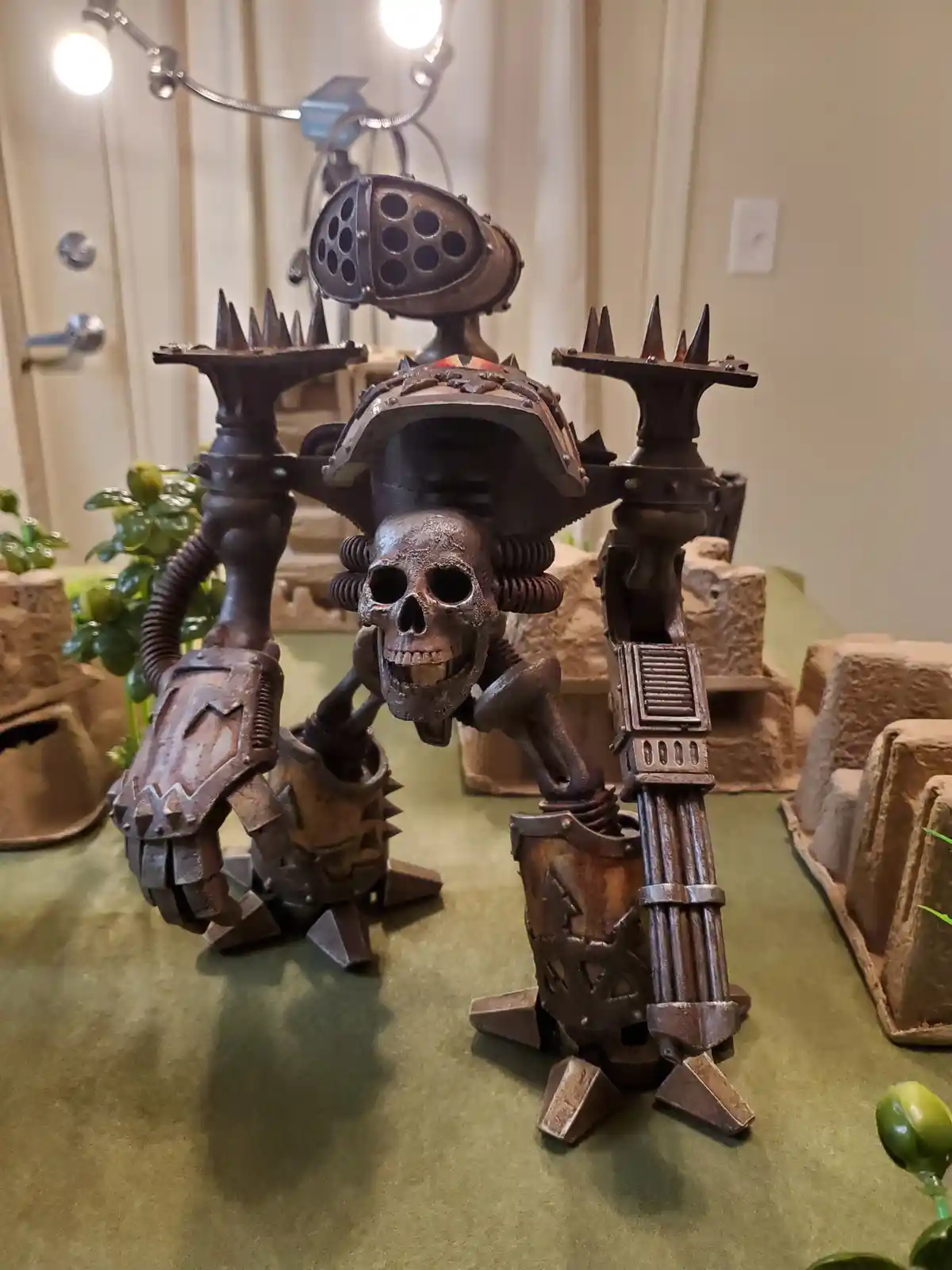 A heavily armored, steampunk-style skeleton robot with spiked arms and a multi-barrelled weapon stands on a green surface…