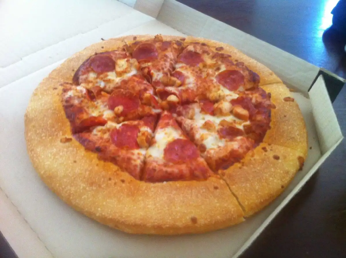 A close-up photo of a pepperoni pizza in an open cardboard box, with the crust forming a thick, golden-brown ring around the…