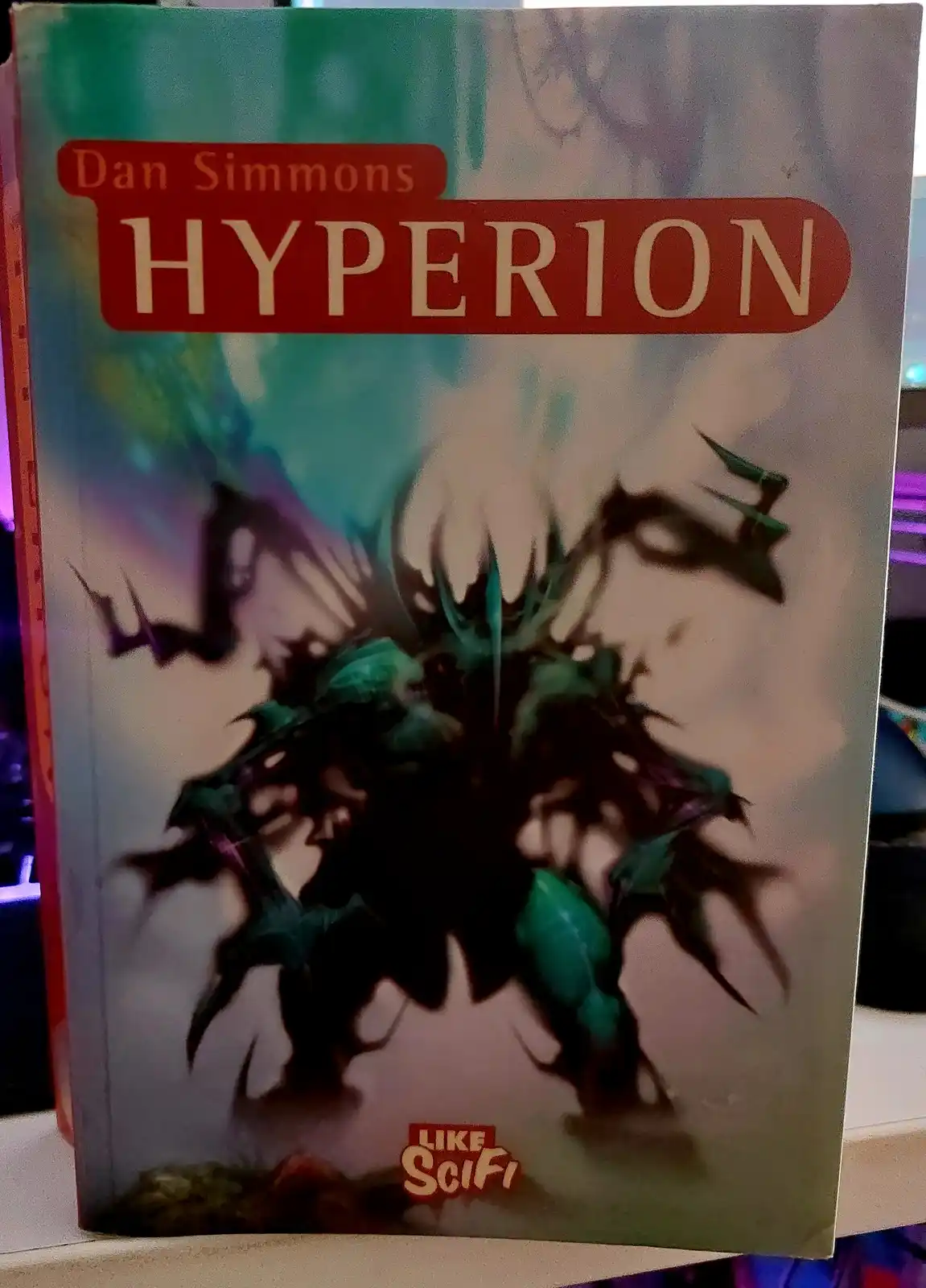 The image shows the cover of Dan Simmons' science fiction novel 'Hyperion', featuring an abstract, spiky, green and black…