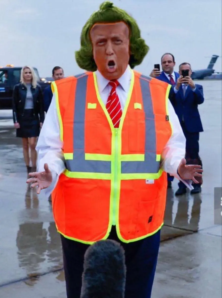 A person wearing a large, exaggerated mask of Donald Trump with green hair, dressed in a bright orange construction safety…