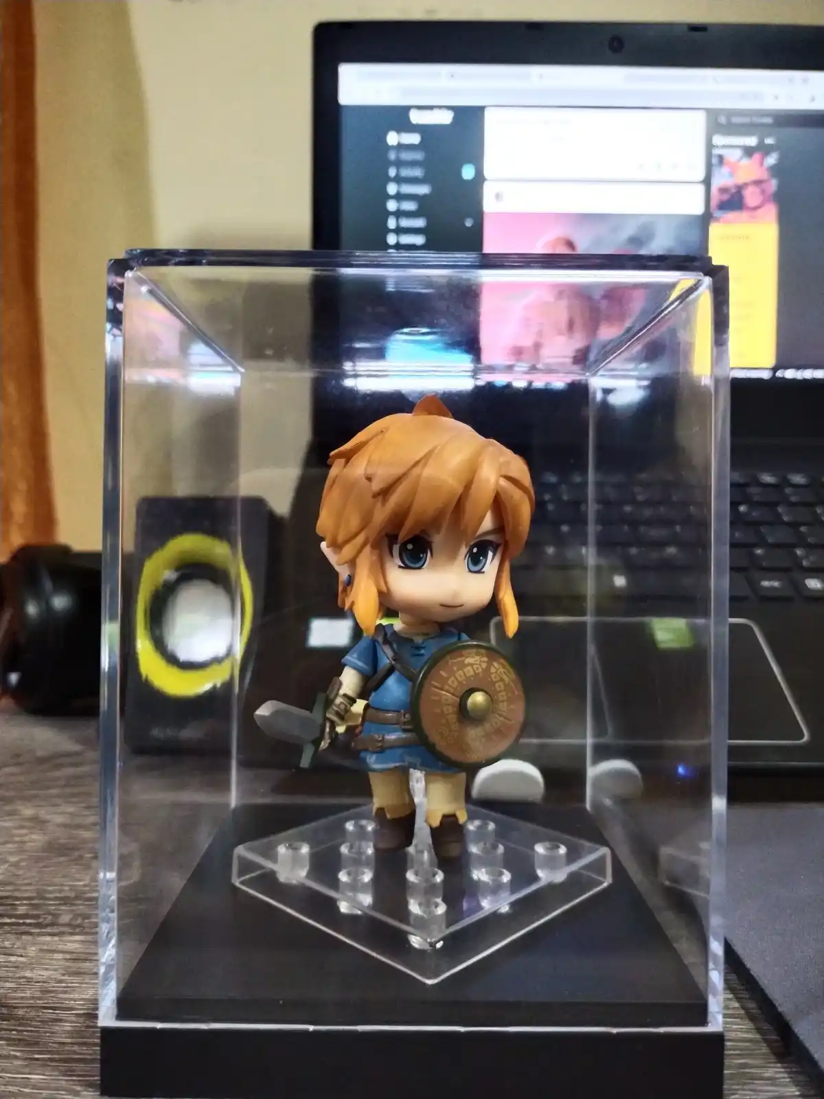 A chibi-style Link figurine from The Legend of Zelda, holding a shield and sword, is displayed inside a clear acrylic case…
