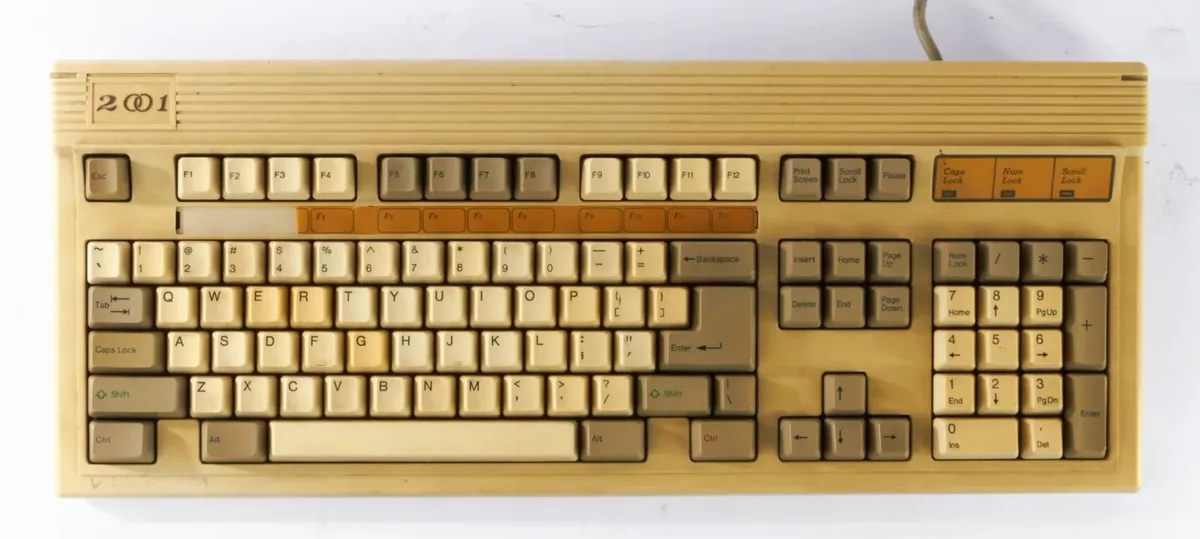 A beige, vintage computer keyboard with a label reading '2001' on its top left corner, featuring a standard QWERTY layout…
