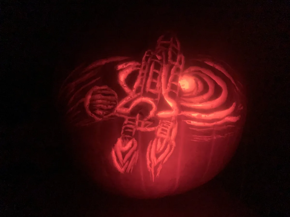 A carved pumpkin illuminated from within, glowing red in the dark, features an intricate design resembling a stylized…