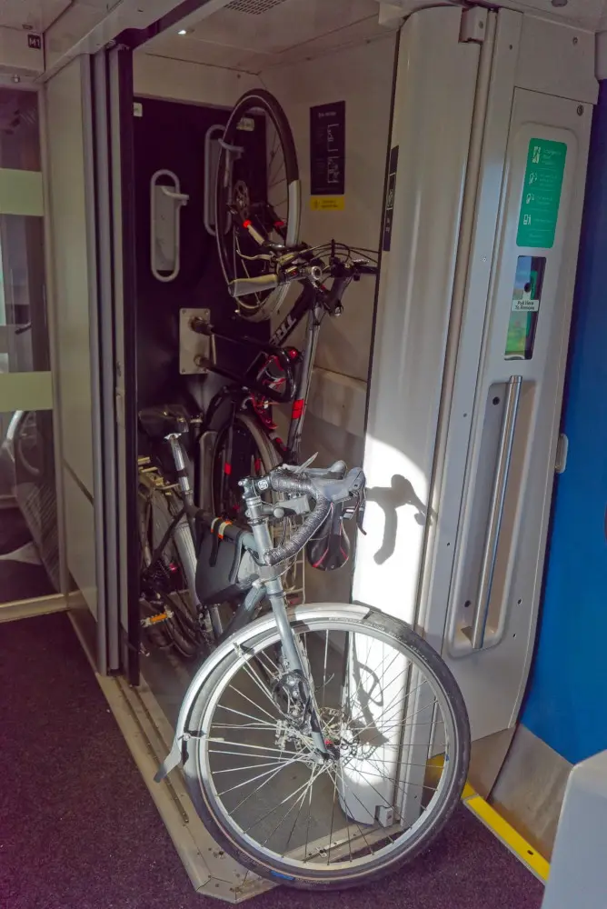 A bicycle is wedged awkwardly in the doorway of a train carriage, partially blocking the entrance while other bikes are…