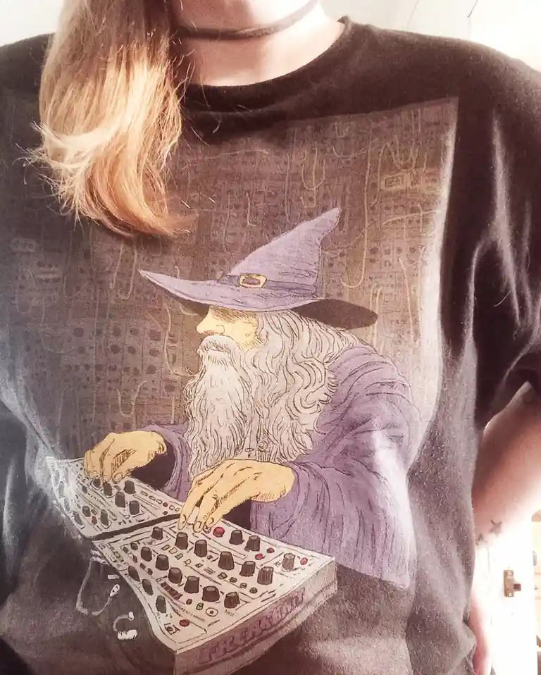 A person wearing a dark grey t-shirt with a graphic of a wizard in a purple robe and hat, depicted as if operating a modern…