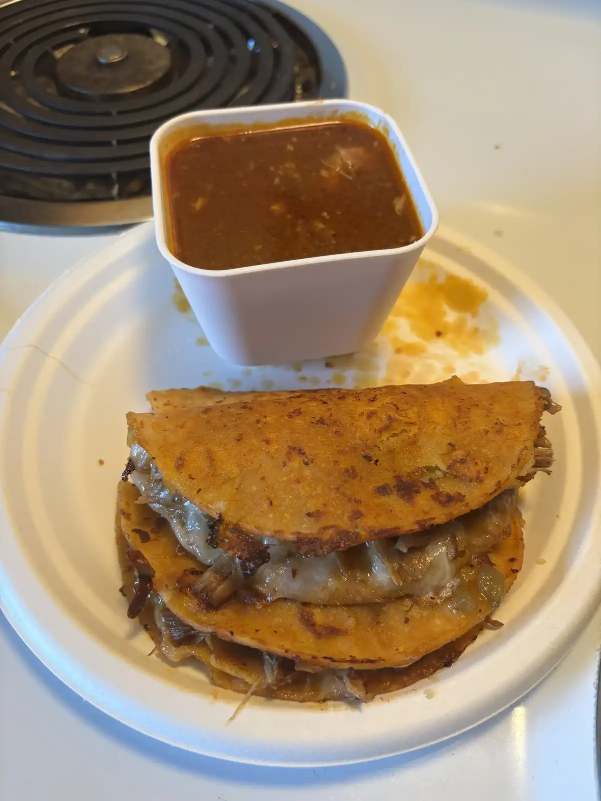 A close-up photo shows a stack of golden-brown, crispy fried tacos on a white paper plate, accompanied by a small white…