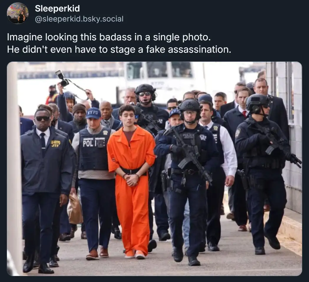 A young man in an orange prison jumpsuit walks calmly with his hands cuffed in front of him, surrounded by a large group of…