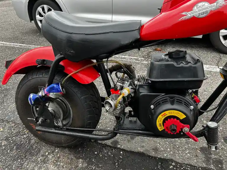 a red baja warrior 200 mini motorcycle is parked in a lot, featuring a black seat, exposed engine, and a red bull energy…