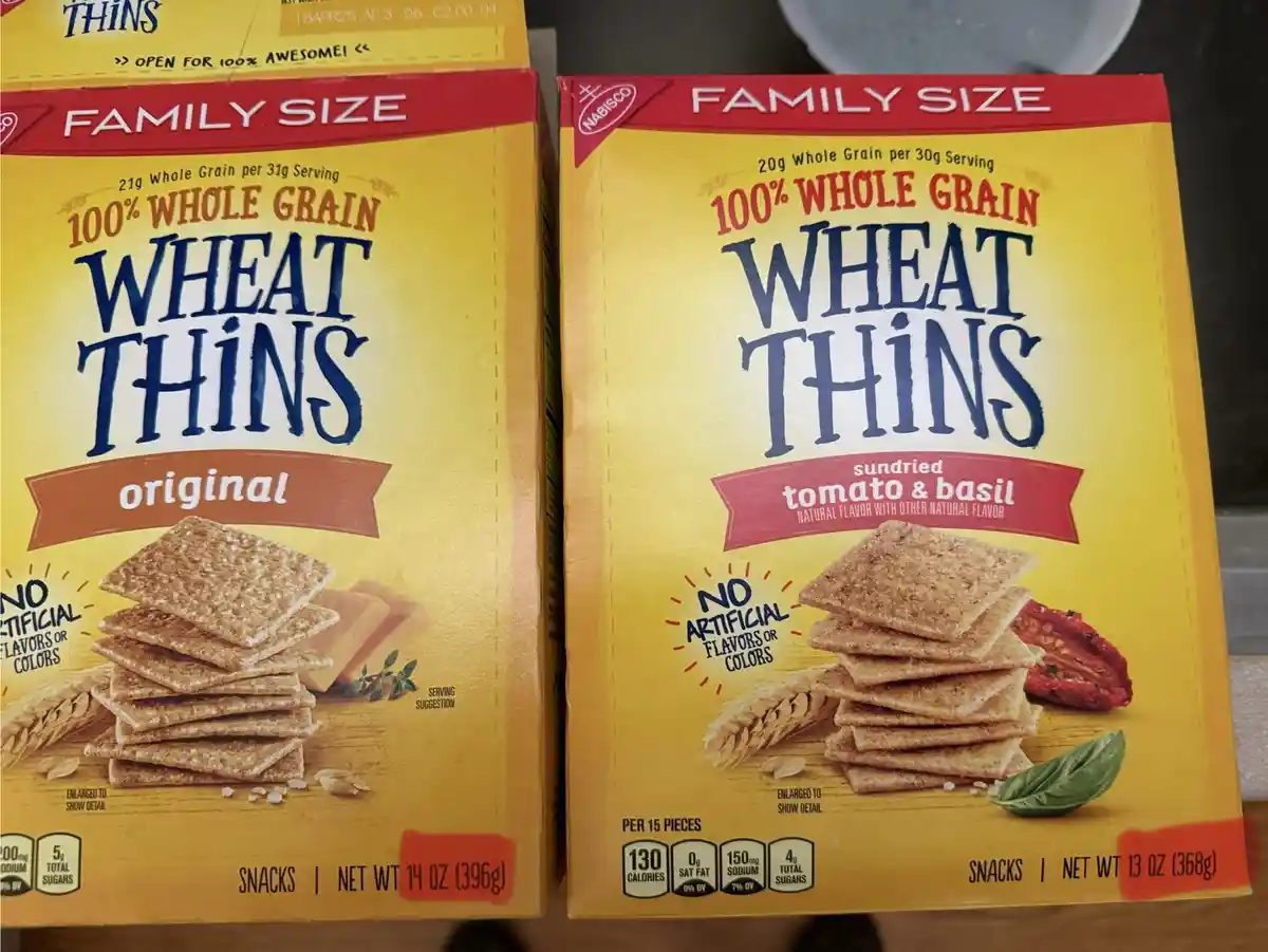 Two side-by-side boxes of Nabisco Wheat Thins, one 'original' and one 'sundried tomato & basil', both labeled 'family size'…