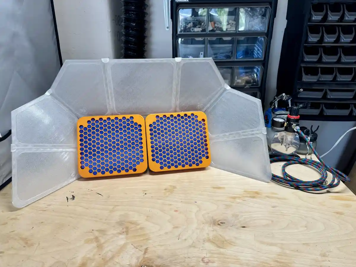 Two orange hexagonal filters with blue honeycomb patterns sit on a wooden workbench, framed by a translucent plastic shield…