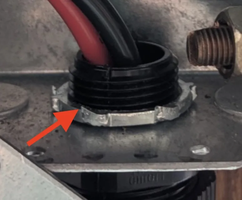 a close-up photo shows a black rubber grommet with red and black wires inserted into it, mounted on a metal plate. A red…
