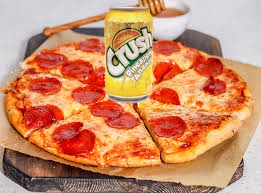 A pepperoni pizza is sliced and served on a wooden board, with a yellow can of Crush soda placed directly on top of the…