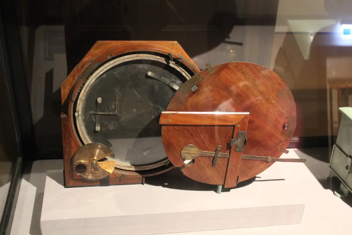 A vintage wooden box with a round glass door and brass fittings, displayed in a museum case, has the overlaid text 'i'm not…