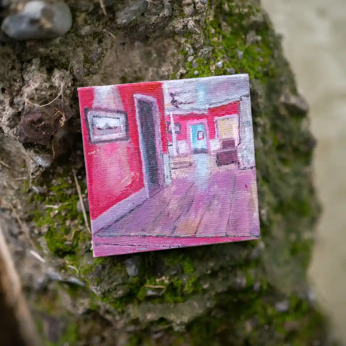 A small, square, textured painting depicting a stylized, abstract hallway with pink and red walls, a dark doorway, and a…