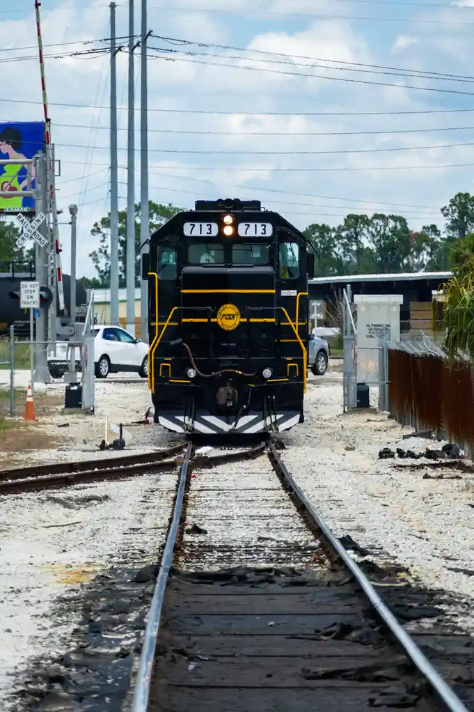 A black Florida Central & Peninsular Railroad locomotive numbered 713 approaches on a gravel-covered track, with a white car…