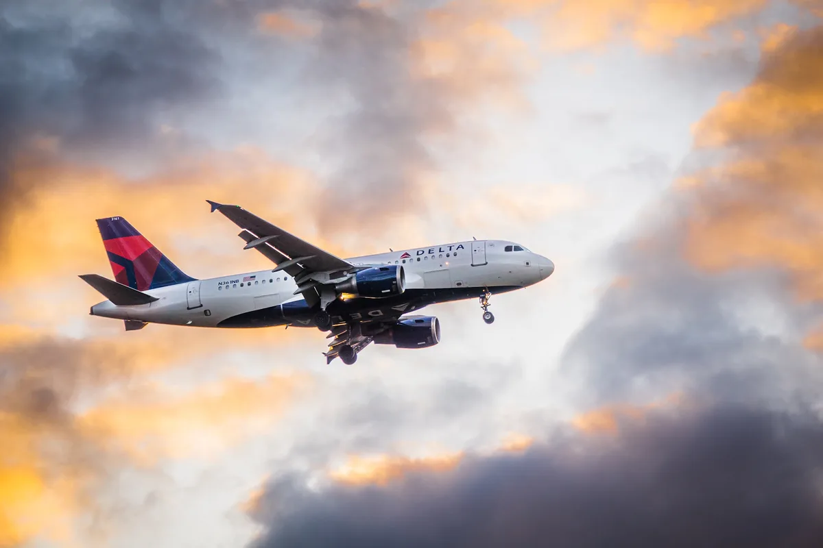 A Delta Air Lines passenger jet, registration N361NB, is captured mid-flight against a dramatic sky of orange and gray…