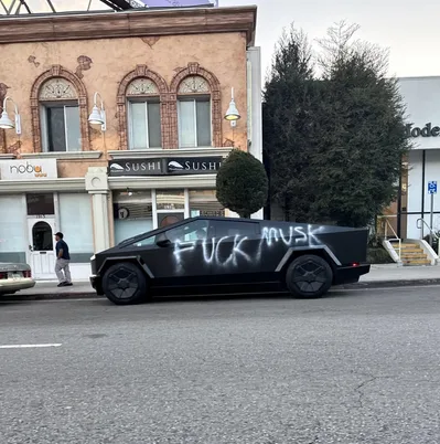 A black Tesla Cybertruck parked on a city street has the words 'FUCK MUSK' spray-painted in large white letters across its…