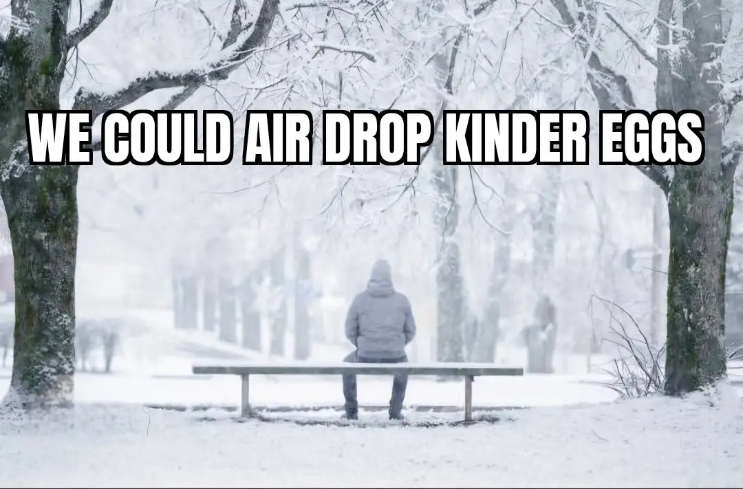 A person in a grey hooded jacket sits alone on a snow-covered park bench, facing away from the camera, surrounded by…