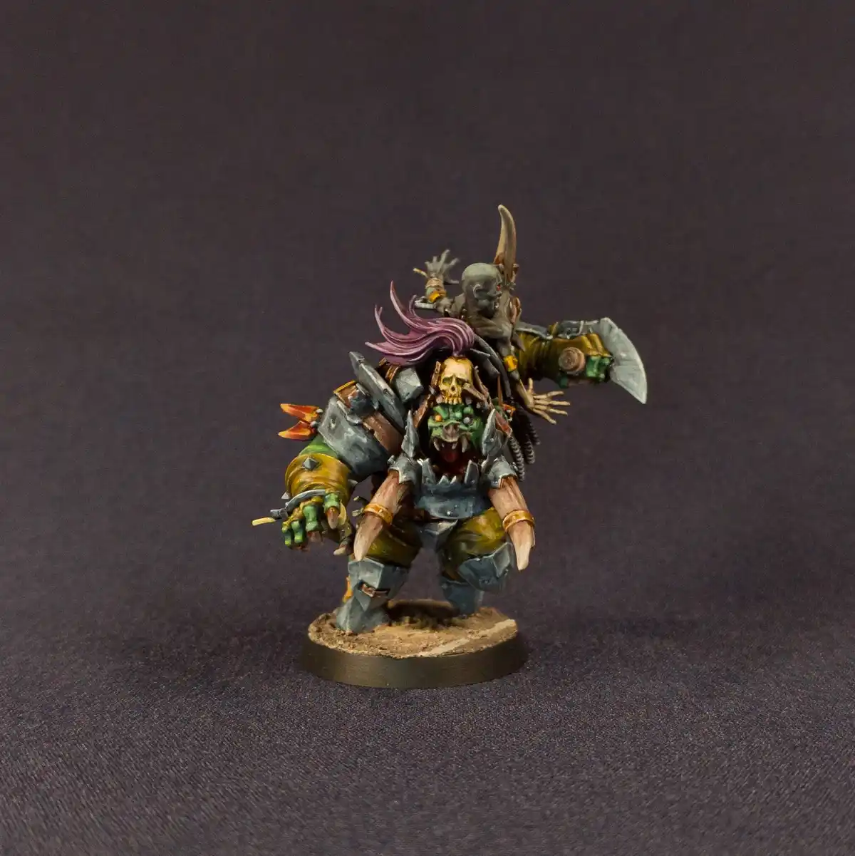 A heavily painted fantasy miniature of a green-skinned, horned warrior with a skull on his chest and purple hair, standing…