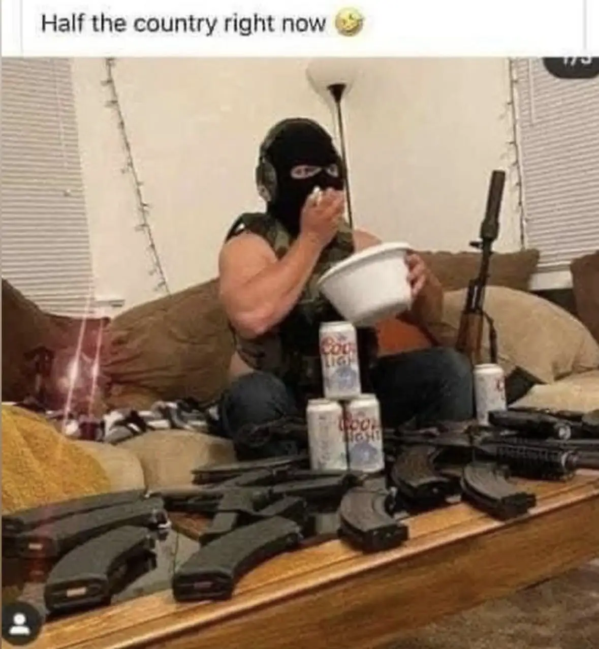 A person wearing a black balaclava and headphones sits on a couch, casually eating from a white bowl while surrounded by…