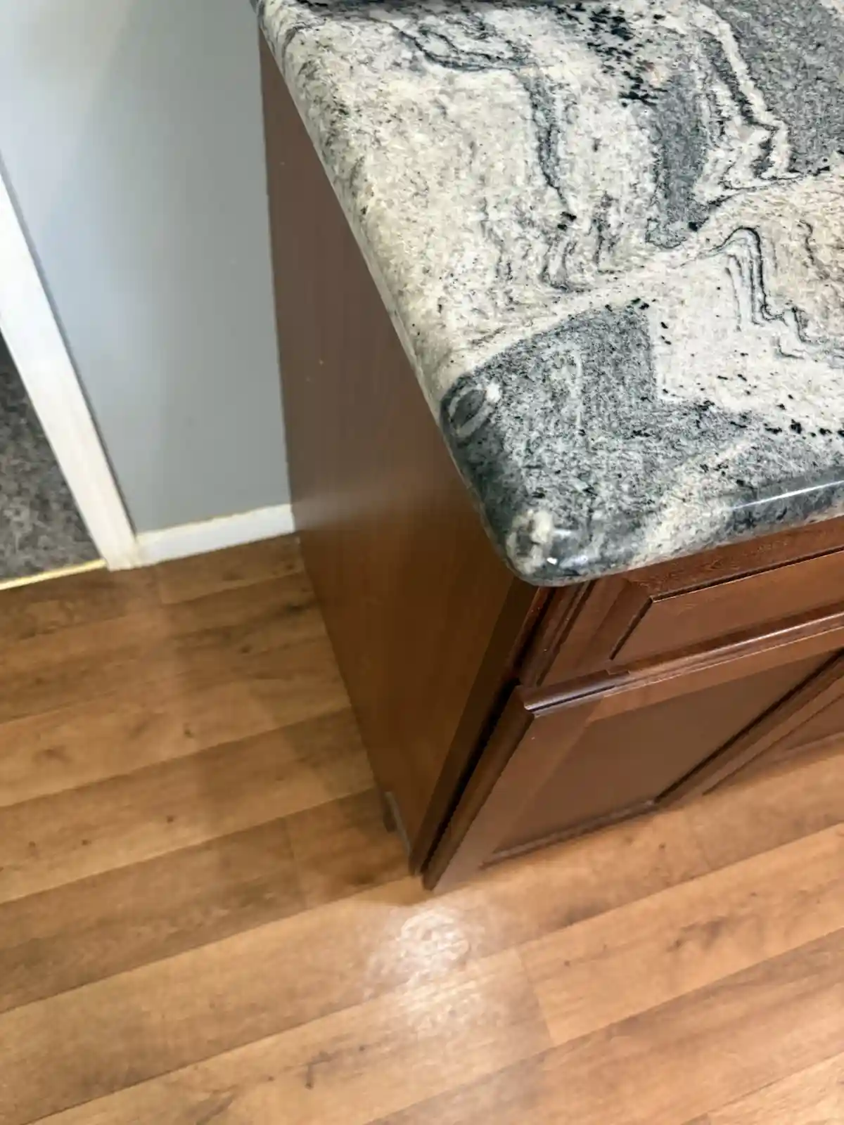 A close-up photo of a granite countertop with gray and black veining, mounted on dark brown wooden cabinets, set against a…