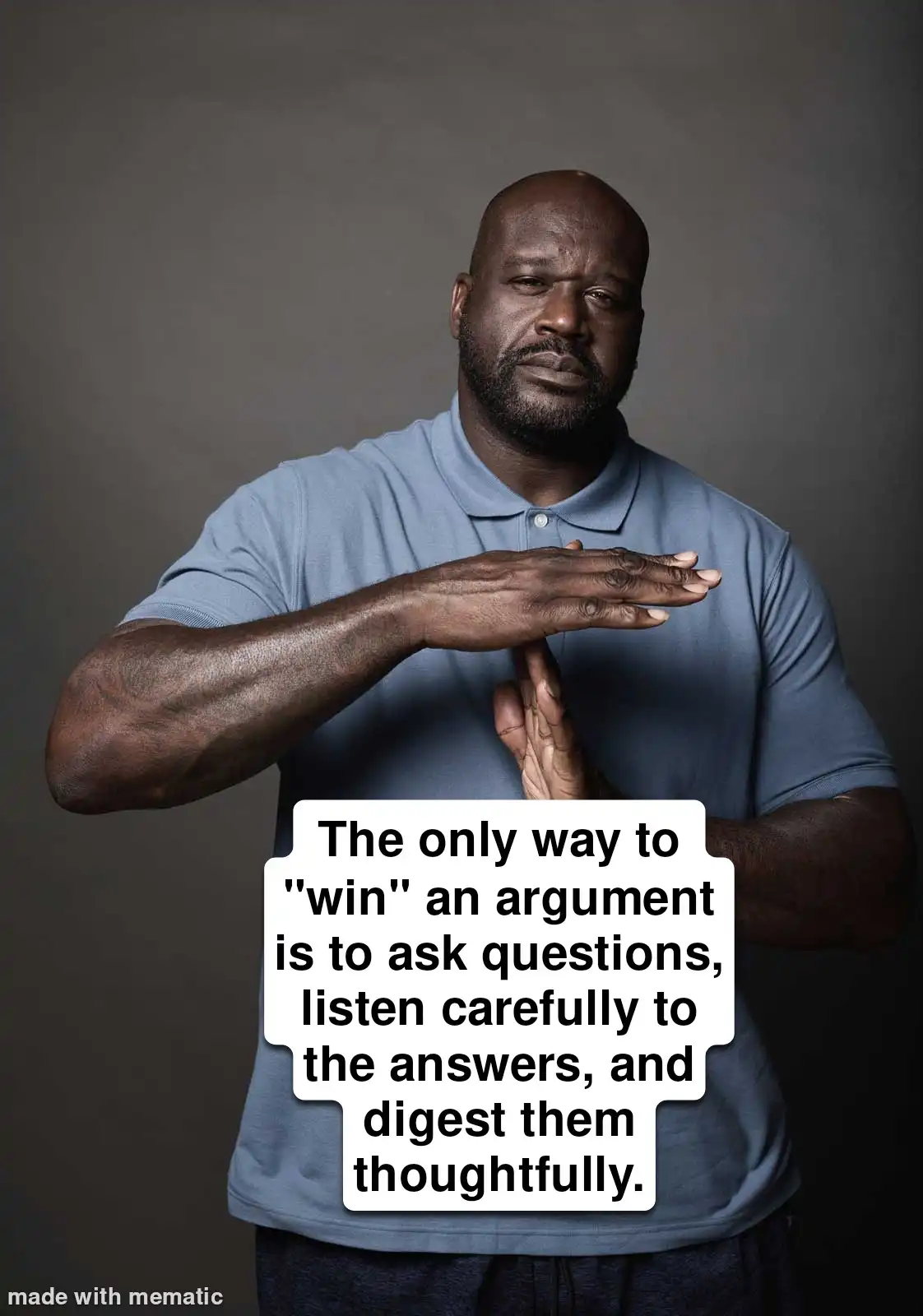 A bald Black man with a beard, wearing a blue polo shirt, stands against a gray background. He makes a gesture with his…