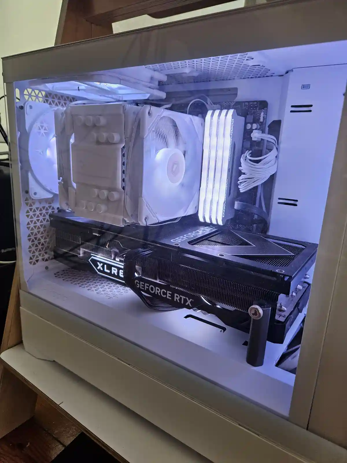A white computer case with a clear side panel shows internal components, including a white CPU cooler with fans and a black…