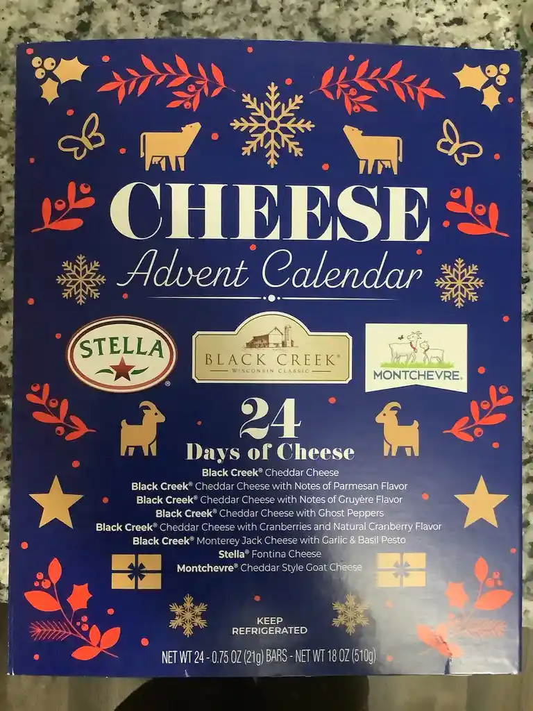 A blue cheese advent calendar box decorated with red holly, gold snowflakes, and goat/cow silhouettes, listing 24 cheese…