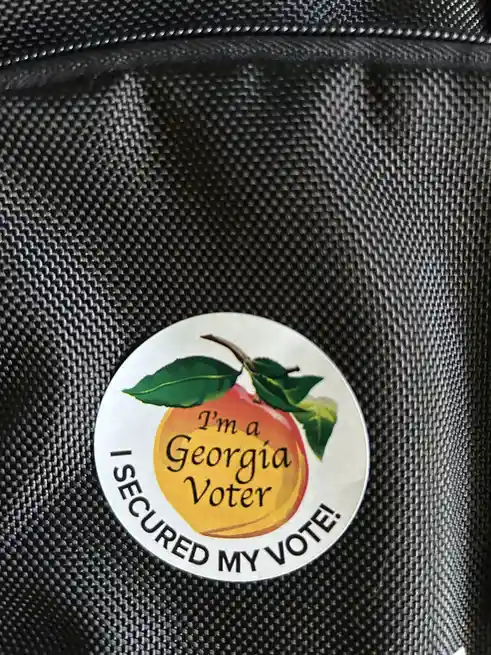 A circular sticker featuring a peach with green leaves and the text 'I'm a Georgia Voter' inside the fruit, and 'I SECURED…
