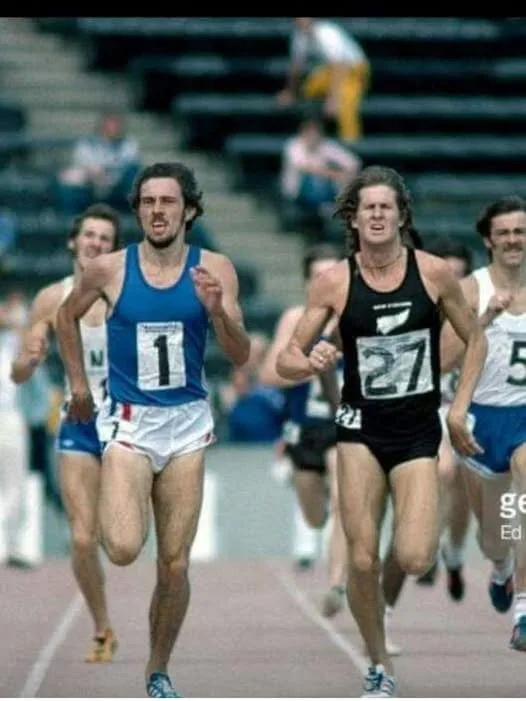 A vintage photo of male track runners in a race, with the runner in the blue jersey (number 1) and the runner in the black…