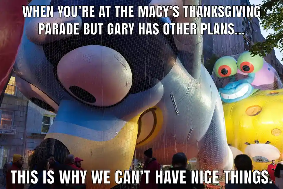 The image shows large, inflated parade balloons, including a prominent blue and yellow one resembling a cartoon character…