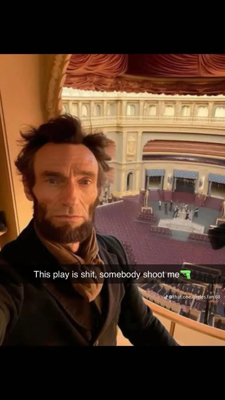 A man dressed as Abraham Lincoln, with his signature beard and dark clothing, takes a selfie from a theater balcony…
