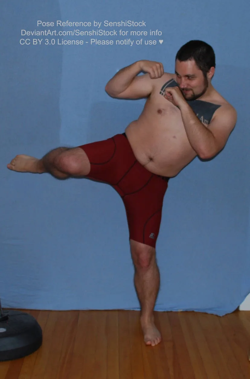 A shirtless man with tattoos on his chest and shoulders is posing in red athletic shorts against a blue backdrop, balancing…