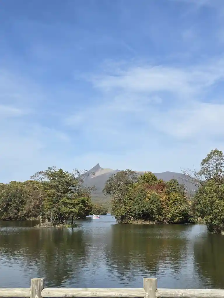 A scenic photo of a calm lake with trees on either side and a mountain in the background under a blue sky. A small…